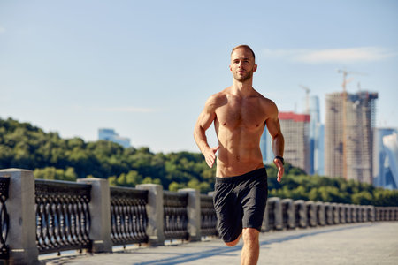 Urban sports. Sporty man shirtless jogging for fitness in the city park on a beautiful summer dayの写真素材
