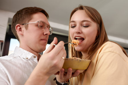 Smiling loving husband feeding wife, young couple enjoying tender moment, romantic date, having fun,...
