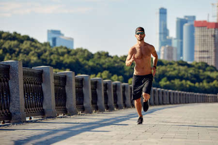 Urban sports. Sporty man shirtless jogging for fitness in the city park on a beautiful summer dayの写真素材