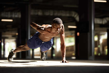 Fitness black man exercising push ups. Male model cross-training in urban background African guy in his twenties doing workout outdoors in the street.の写真素材