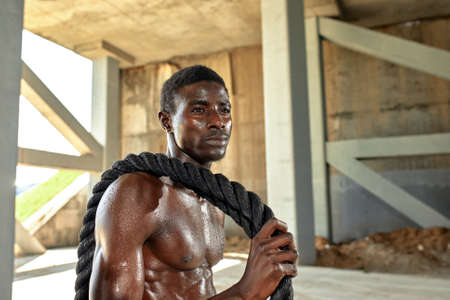 Rope workout. Sport man doing battle ropes exercise outdoor. Black male athlete exercising, doing functional fitness training with heavy ropeの写真素材