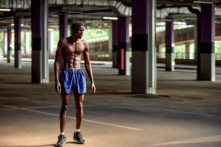 Handsome afro American sportman standing on the street while taking break after training. Black male having rest after workoutの写真素材