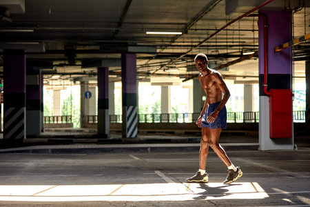 Handsome afro American sportman standing on the street while taking break after training. Black male...