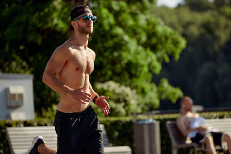 Urban sports. Sporty man shirtless jogging for fitness in the city park on a beautiful summer dayの写真素材