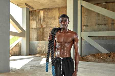 Rope workout. Sport man doing battle ropes exercise outdoor. Black male athlete exercising, doing functional fitness training with heavy ropeの写真素材