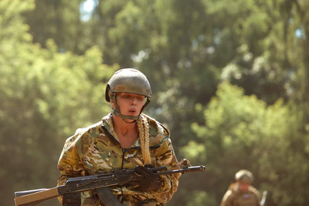 Caucasian Military lady woman in tactical gear posing for photo at summer season. Wearing green camo...