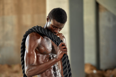 Athlete man with a battle rope doing sports exercises outdoor. Black male athlete exercising, doing functional fitness training with heavy ropeの写真素材