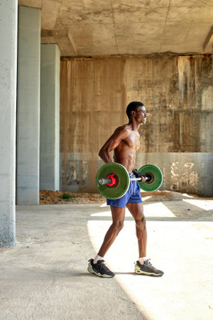 Athletic black young man lifting a heavy-weight barbell in outdoor gym under the bridge. Healthy lifestyle conceptの写真素材