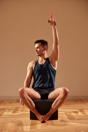 Handsome pilates male instructor performing stretching balance fitness exercise on small barrel...