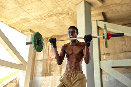 Athletic black young man lifting a heavy-weight barbell in outdoor gym under the bridge. Healthy lifestyle conceptの写真素材