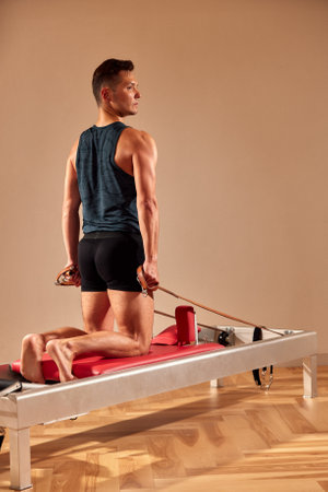 Side view of barefoot male athlete lying on pilates reformer and performing abs exercise during fitness workout. Pilates man concept.の写真素材
