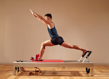 Fit man doing a lunge stretch yoga pilates exercise to strengthen and tone his muscles using a reformer in gym. Health and fitness conceptの写真素材
