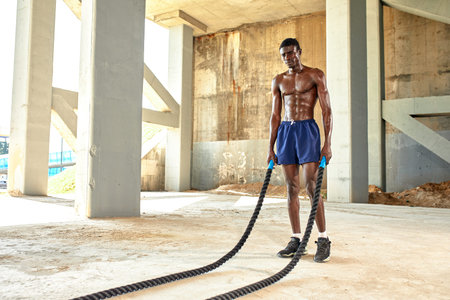 Rope workout. Sport man doing battle ropes exercise outdoor. Black male athlete exercising, doing...