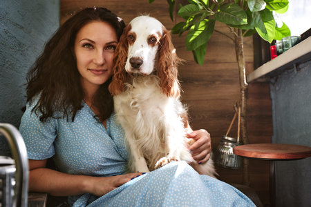 Cheerful young woman holding her big puppy with black nose and laughing. Indoor portrait of smiling...