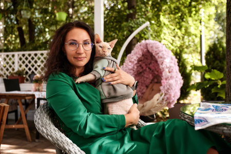 A young woman sits at a table at an outdoor cafe bar and plays with the cat.の写真素材