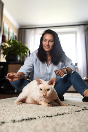 Playing with cat at home. Young woman lying on the floor and hugging pet.