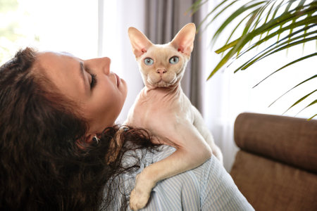 Playing with cat at home. Young woman sitting on couch and hugging pet.の写真素材