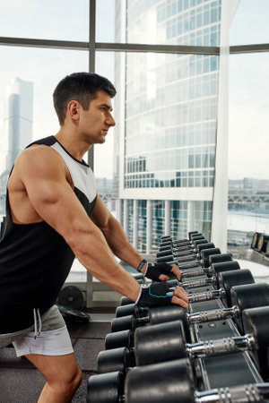 Man doing exercise with dumbbell in the gym. Photo of a sexy muscular man in sportswear and good physique on grey background. Strength and motivation, sport, fitness goalの写真素材