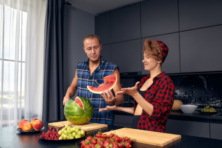 Happy couple standing in kitchen at home preparing together yummy dinner on first dating, spouses chatting enjoy warm conversation and cooking process, caring for health, eating fresh vegetable saladの写真素材