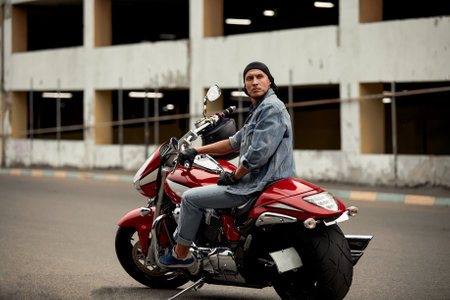 Lifestyle of a motorcyclist, a handsome biker with long hair on a red classic bike in an urban landscape.の写真素材