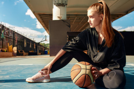 A basketball player is sitting on a sports field with a basketball and looks away. Sports, fitness, lifestyleの写真素材