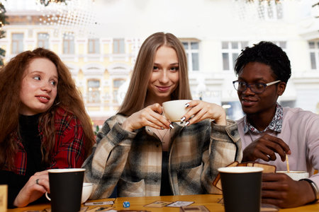 Smiling african american guy showing funny video or party photos on smartphone for diverse best friends, group of happy mixed race students meeting in cafe, laughing, sitting at table.の写真素材