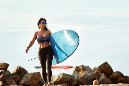 Woman surfer with surfboard going to surf at seaside. Girl holding surfboard o and goes to the ocean...