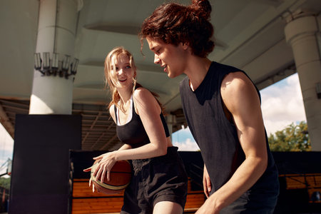Athletic young people play streetball on the street, a girl and a guy play basketball on the city playground.の写真素材
