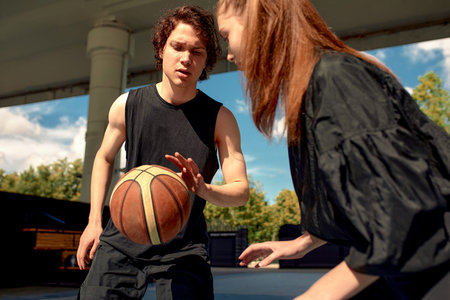 Athletic young people play streetball on the street, a girl and a guy play basketball on the city playground.の写真素材