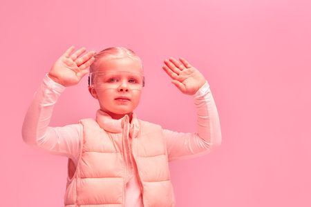 Girl in futuristic clothes and vr glasses is experiencing cyberspace with pink neon light in on pink backgroundの写真素材