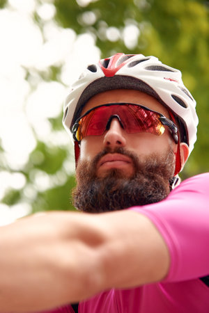 Strong Male cyclist in sportswear, glasses and protective helmet walking with his bike in the forest to take a break after riding. Sky blue in the background.の写真素材