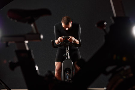 Portrait of a man on an exercise bike in the gym, a man with a beard and glasses on an exercise bike. Fitness man using exercise bike during cardio workout in crossfit gym.の写真素材