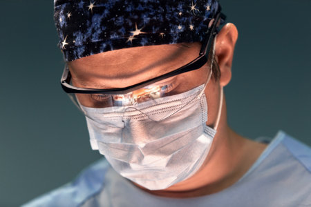The doctor performs an operation in a dark operating room with a lamp in the background, a professional surgeon during a stressful operation.の写真素材