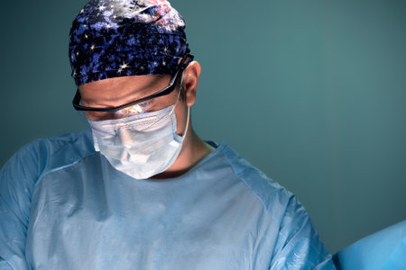 Doctor performing surgery in dark operation room with lamp on backgroundの写真素材