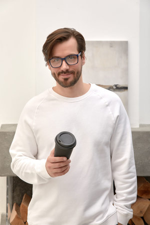 Young handsome man with beard in casual sweater with glass of coffee and glasses happy face smiling...