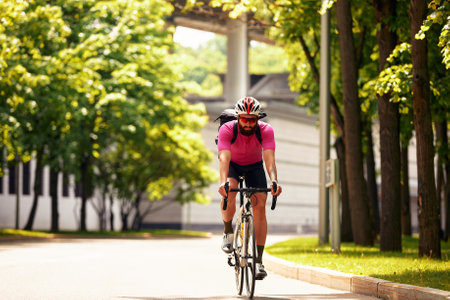 Strong Male cyclist in sportswear, glasses and protective helmet walking with his bike in the forest to take a break after riding. Sky blue in the background.の写真素材