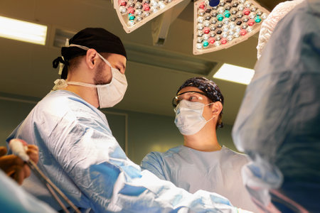The faces of doctors surgeons in masks are a big plan, an operating room, a surgeon performs an operation in a modern operating room with life support devices and light lamps, saving lives, cancer is not a sentence.の写真素材