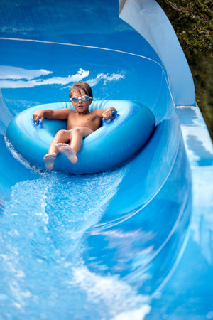Joyful boy descends on an inflatable circle from the water slide in the water park, childrens...