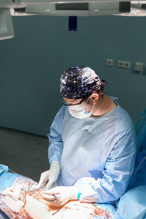 The doctor performs an operation in a dark operating room with a lamp in the background, a...