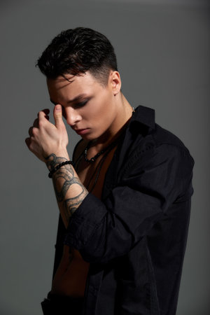 Studio portrait of a young teenager brunette boy in a black shirt with a tattoo on his arm, a pendant and a bracelet. Elegant sexy style. Gray background.の写真素材