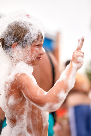 Happy little boy with foam on his head having fun in a water park, in wet swimwear at a foam party or holiday on a sunny hot summer dayの写真素材