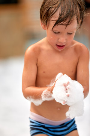Enthusiastic joyful boy at the foam party, close-up of a kid among the foam, foam party for the little oneの写真素材