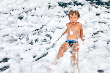 Enthusiastic joyful boy at the foam party, close-up of a kid among the foam, foam party for the little oneの写真素材