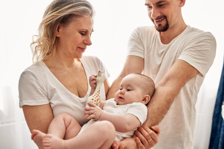 Mom and dad are playing with their little child in a bright room, all dressed in white t-shirts....