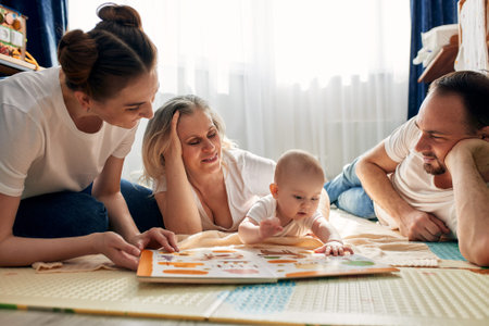 Parents together with their child play and study a childrens book, lying on the floor in a bright...