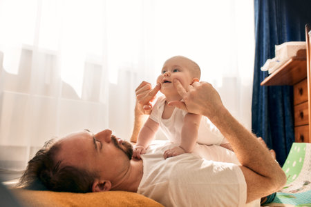 Happy dad holds his newborn baby in his arms while lying on the floor in a bright childs room. The...
