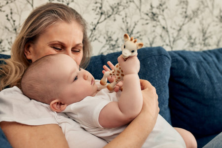 A loving mother holds her child in her arms, who plays with a toy giraffe. Maternal love, learning...