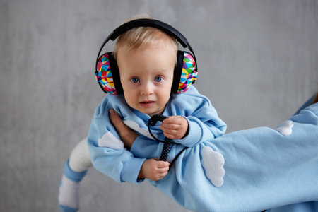 A happy young mother holds her precious baby in her arms. The kid looks into the camera with gray eyes and cheerful multi-colored DJ headphones on his head.の写真素材