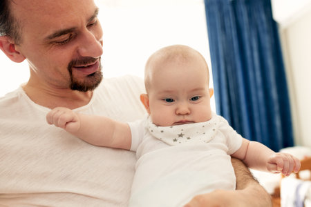 Close-up portrait of happy young father hugging and kissing his sweet adorable newborn child. Indoors shot, concept image. Copy space.の写真素材