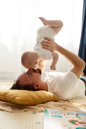 Happy dad holds his newborn baby in his arms while lying on the floor in a bright childs room. The...
